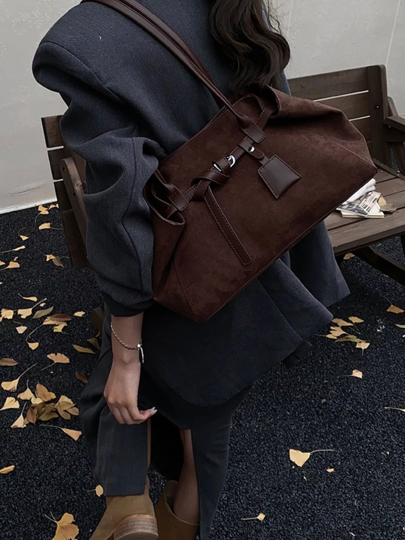 Brown suede shoulder bag with leather strap detail and a small tag.