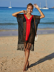 Black crochet cover-up with red V-neck trim and fringe hem, worn on the beach.