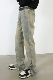Light wash denim jeans with distressed details and split hems with zippers.