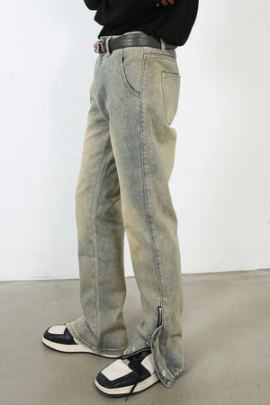 Light wash denim jeans with distressed details and split hems with zippers.