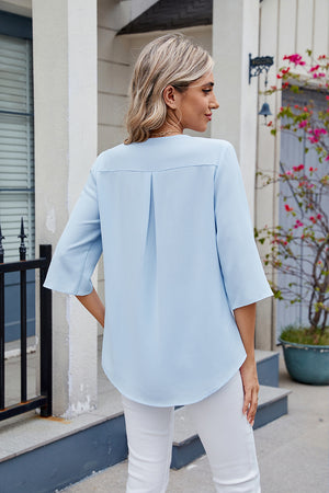 Light blue V-neck flutter sleeve blouse with back pleats and curved hem.