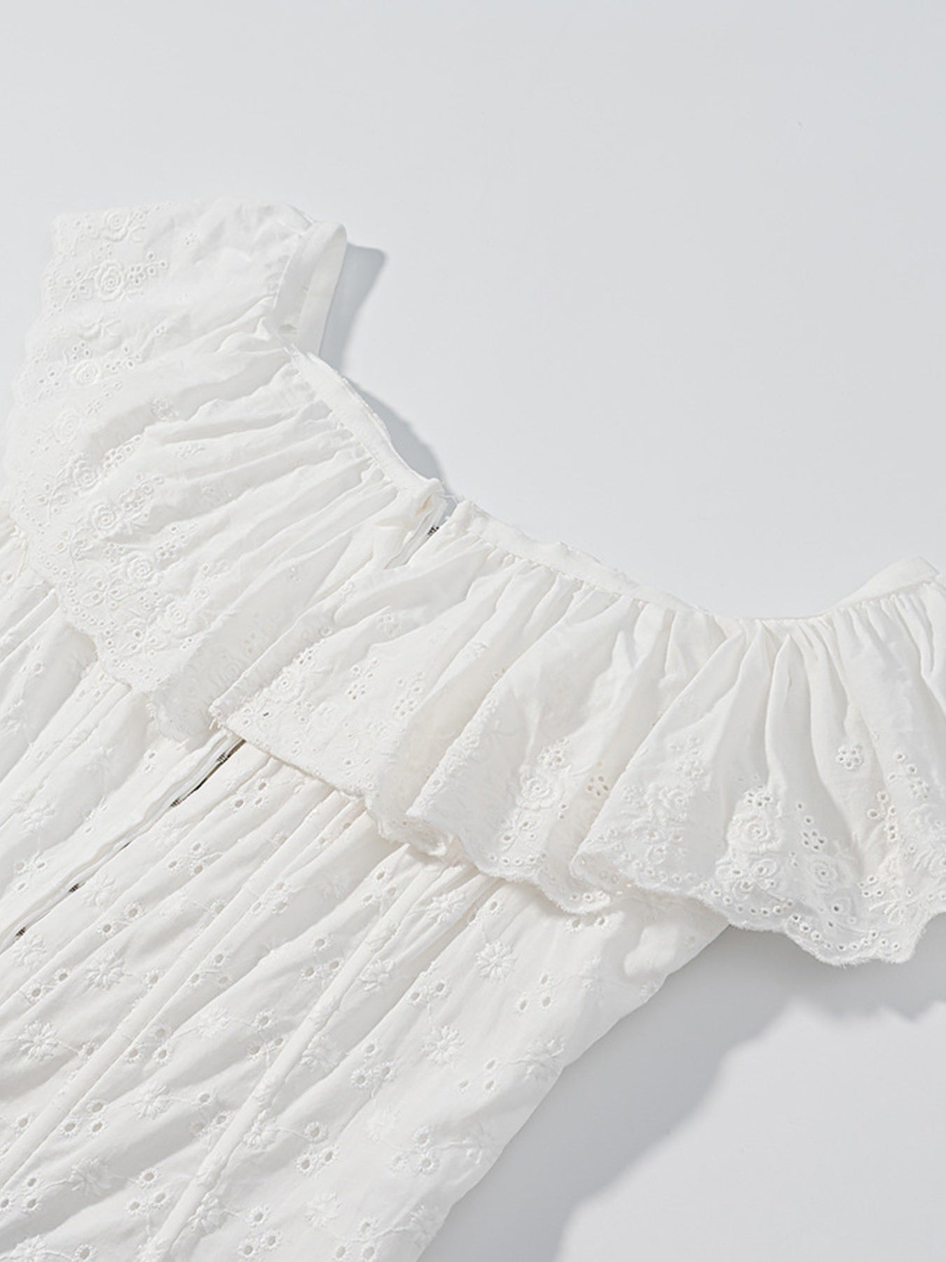 White eyelet tank top with ruffled neckline and delicate floral embroidery.