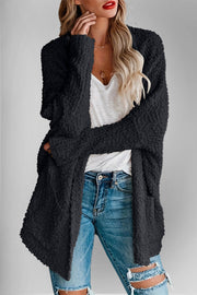 Black popcorn knit open cardigan with pockets, worn over a white top and ripped jeans.