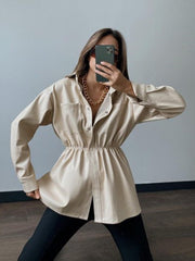 Tan faux leather shirt jacket with gathered waist and button front, styled with a gold chain necklace.