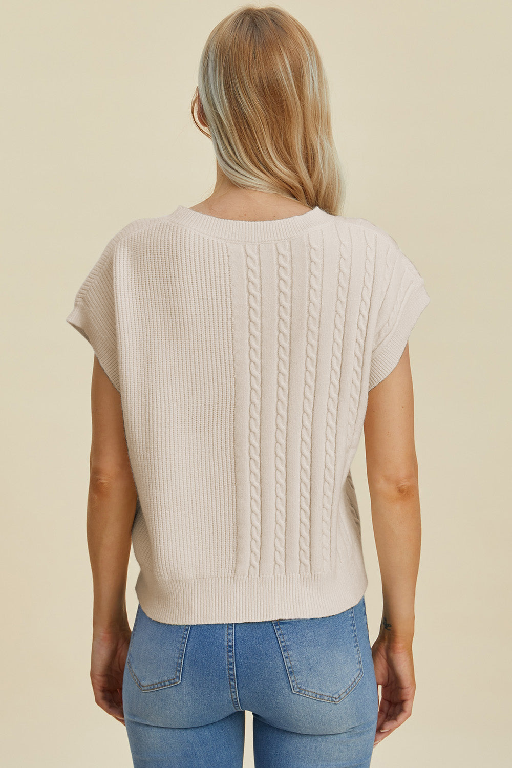 Beige cable knit cap sleeve pullover sweater with ribbed and cable knit panels.