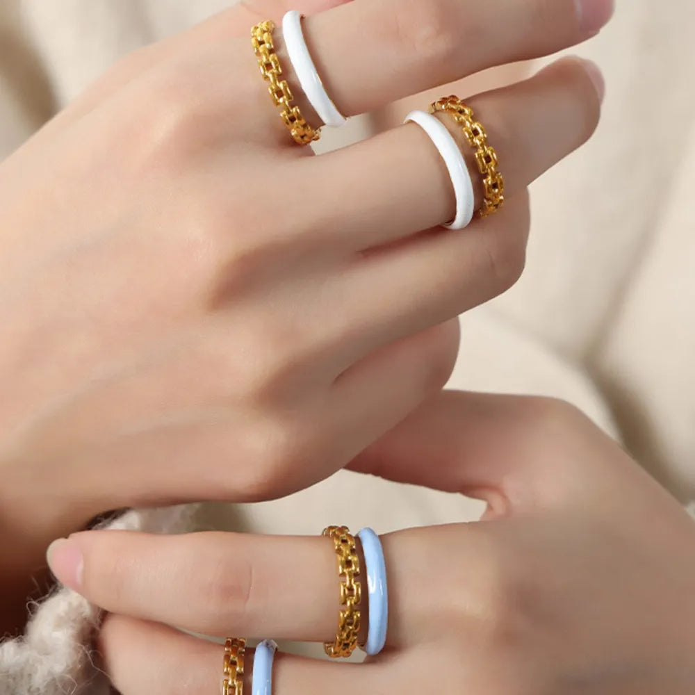 Gold chain link open rings with white and light blue enamel bands stacked on fingers