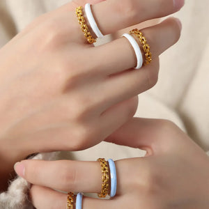 Gold chain link open rings with white and light blue enamel bands stacked on fingers