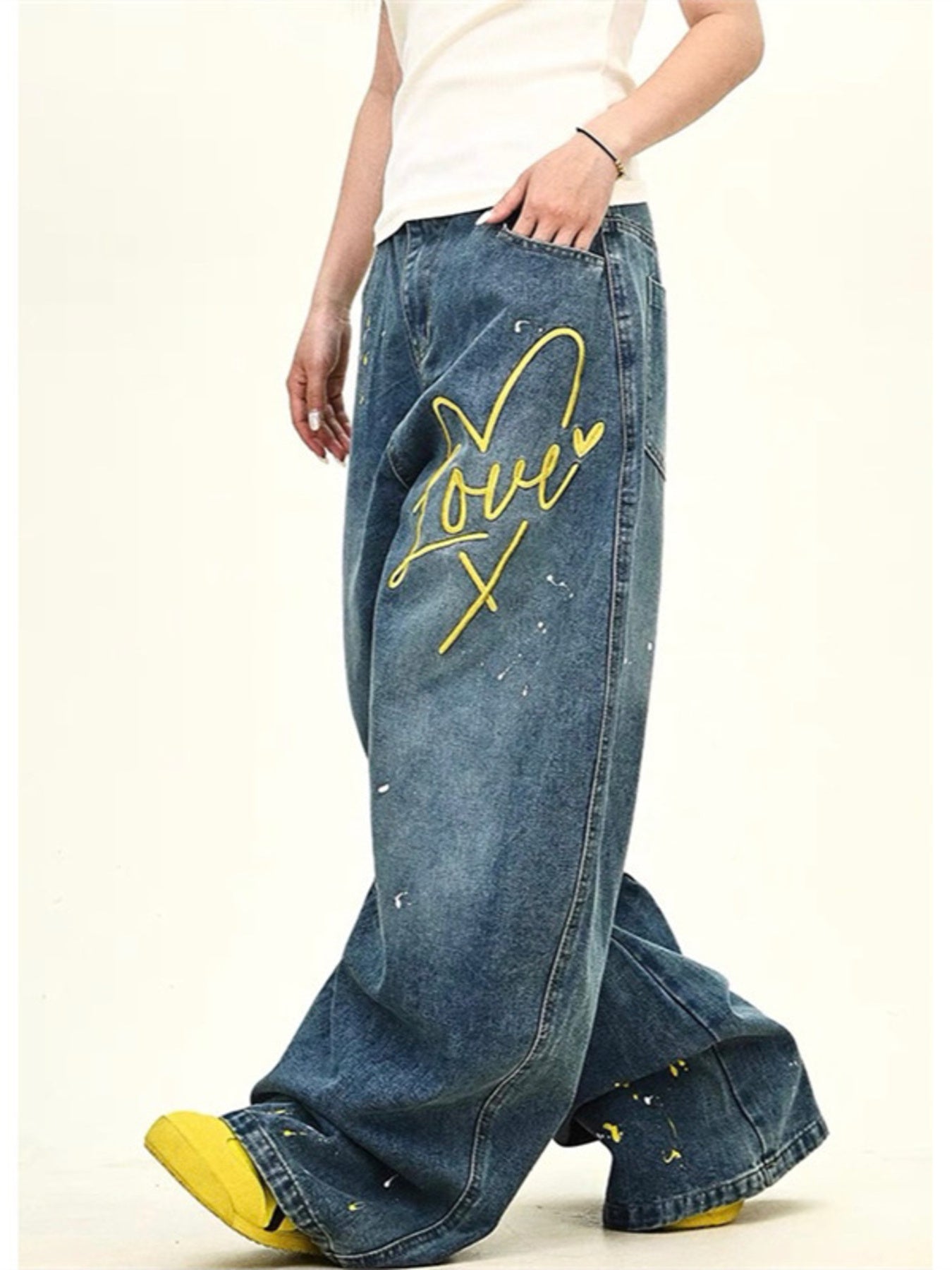 Oversized wide-leg jeans in blue denim with yellow embroidered "Love" graphic and paint splatters.