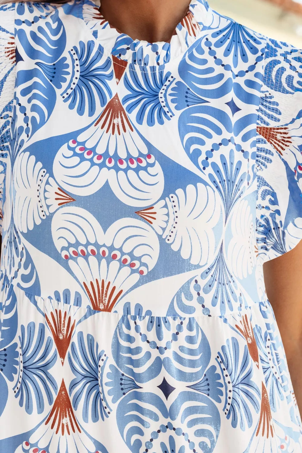 White and blue botanical print ruffled dress with flutter sleeves and tiered skirt detail.