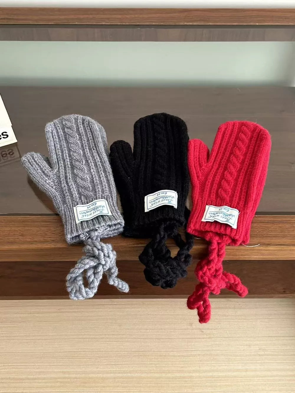 Cozy cable knit acrylic mittens in gray, black, and red with braided detail and attached cords.