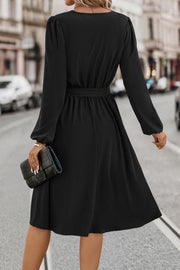 Black midi dress with poet sleeves, a belted waist, and a flowing skirt.