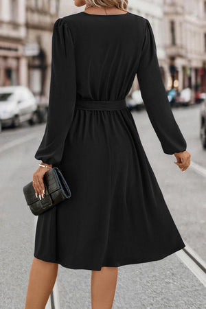 Black midi dress with poet sleeves, a belted waist, and a flowing skirt.