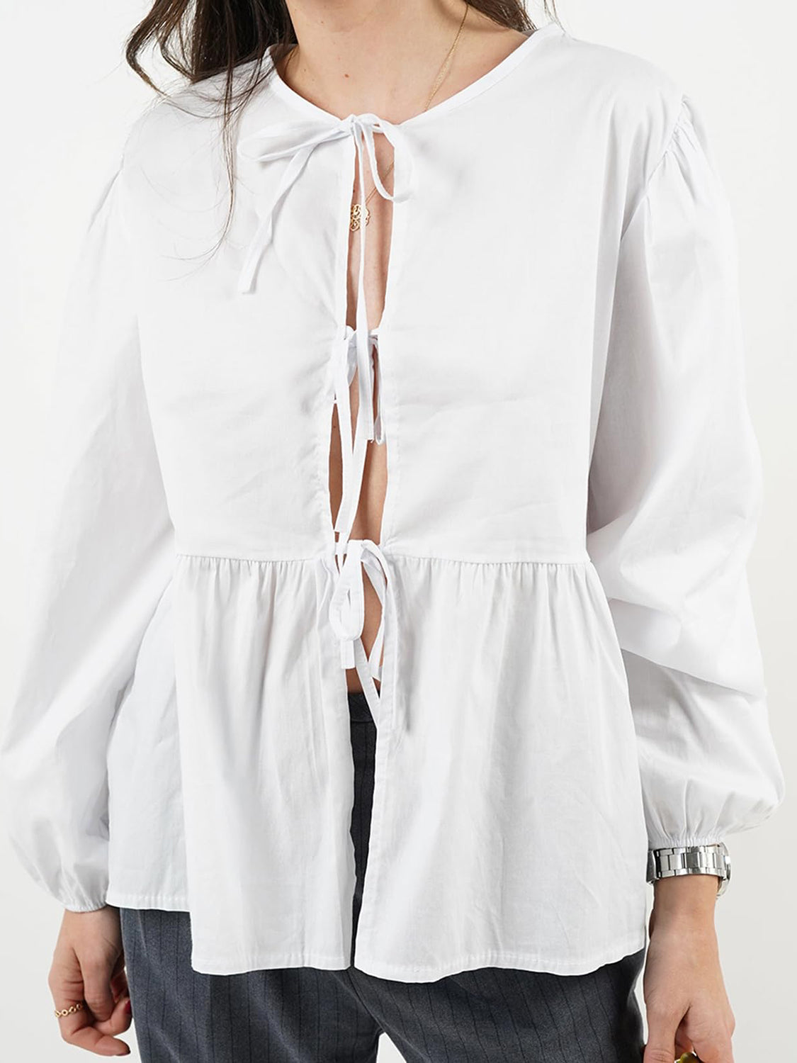 White tie-front peplum blouse with voluminous sleeves and a ruffled hem.