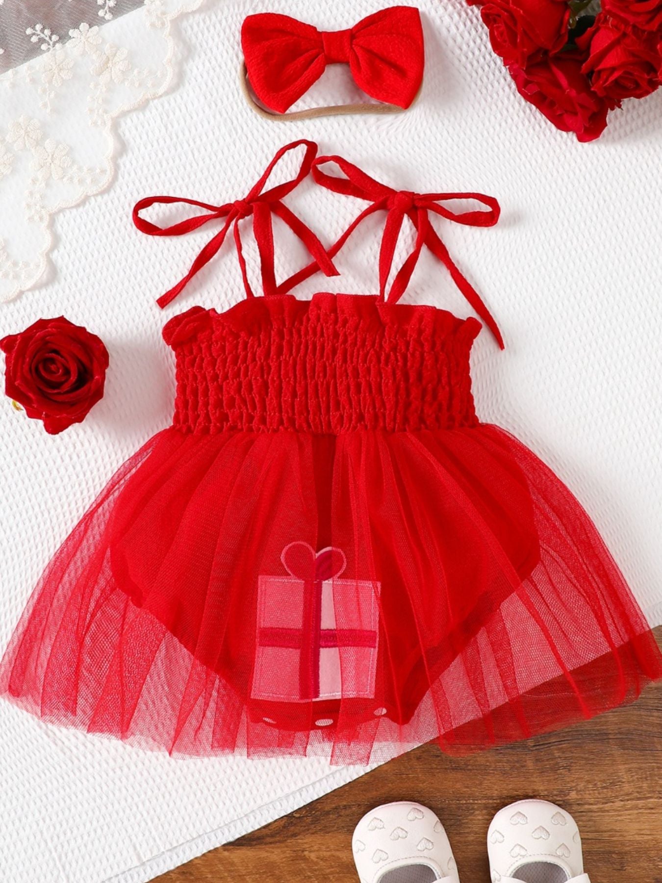 Red baby bodysuit dress with smocked bodice, tulle skirt, gift applique, and tie straps.