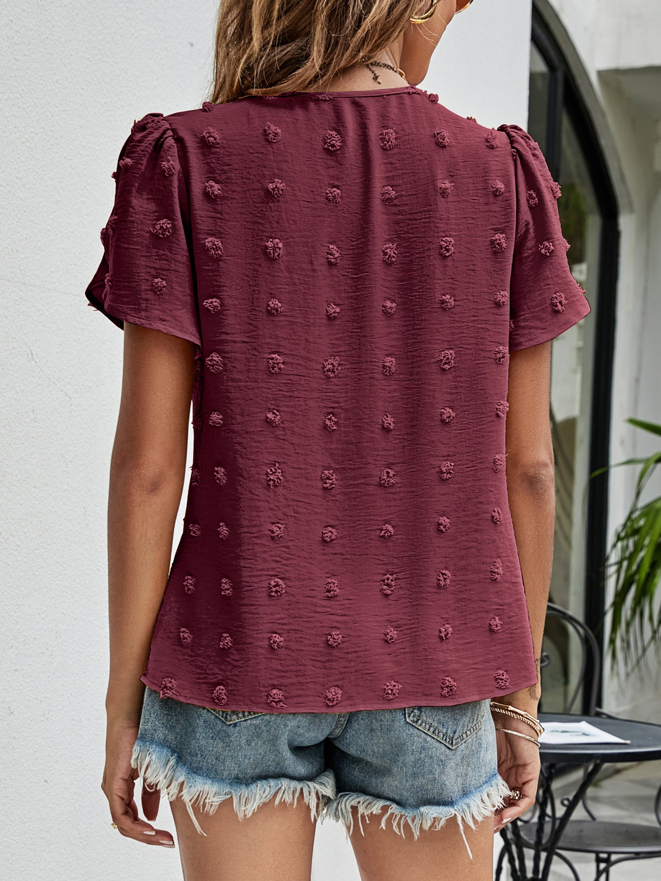 Textured puff sleeve wine blouse with dot pattern and V-neck, styled with denim shorts.
