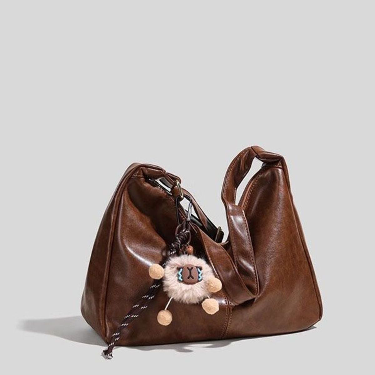 Brown vintage hobo shoulder bag with fluffy sheep charm and braided strap detail.