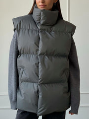Padded puffer vest in Dark Gray with a high collar and sleeveless design, worn over a gray sweater.
