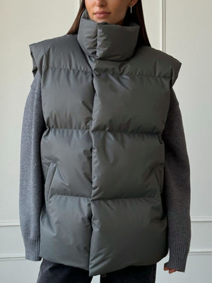 Padded puffer vest in Dark Gray with a high collar and sleeveless design, worn over a gray sweater.
