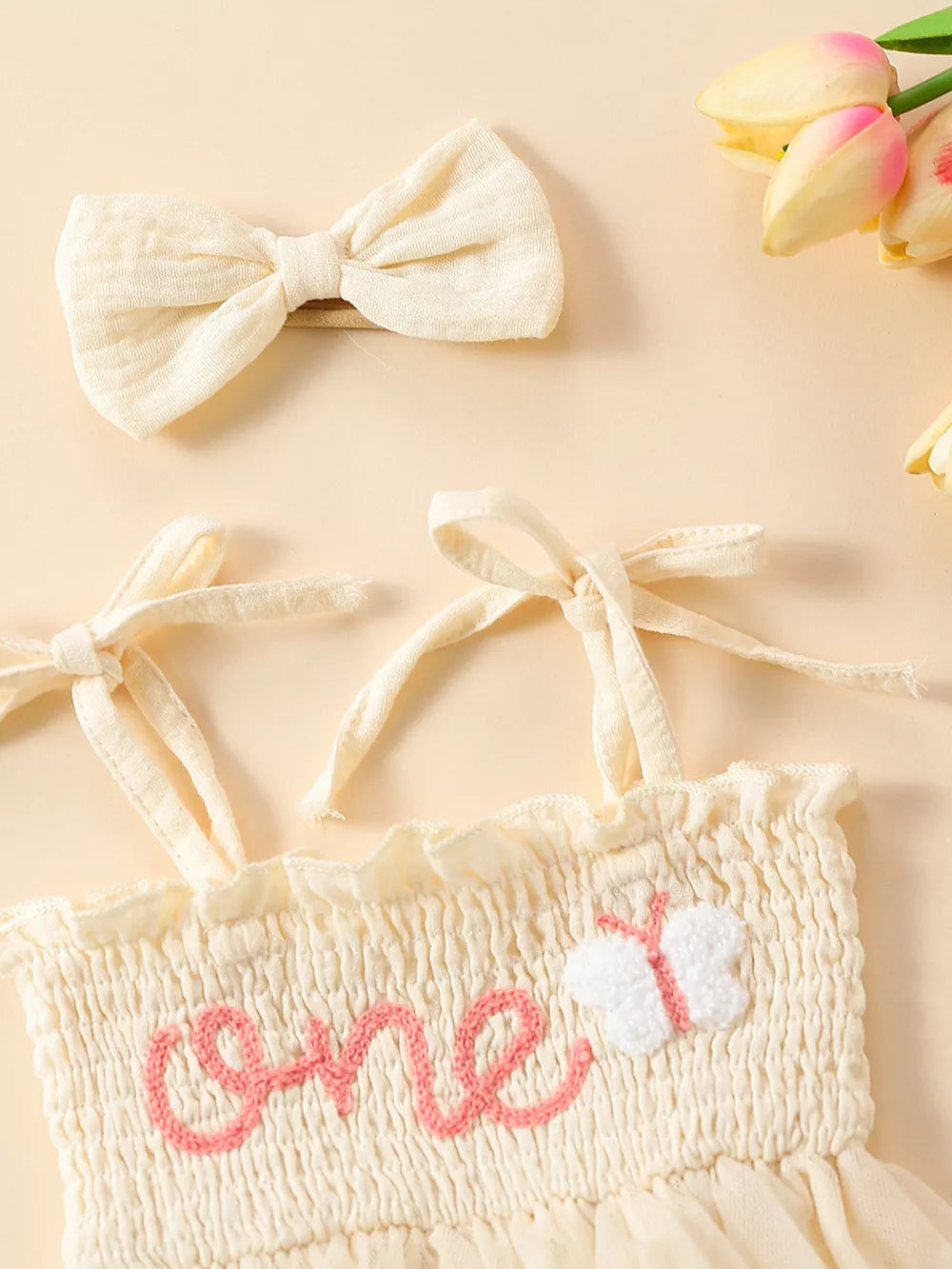 Apricot smocked baby bodysuit with pink "one" embroidery and butterfly detail, with matching bow headband.