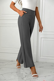 Dark gray wide-leg trousers with a sculpted waist and pockets, styled with white heels.
