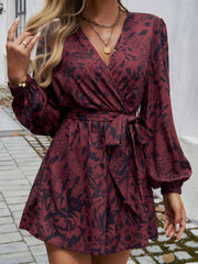 Floral wrap romper in dark brown with blouson sleeves and a tie waist.