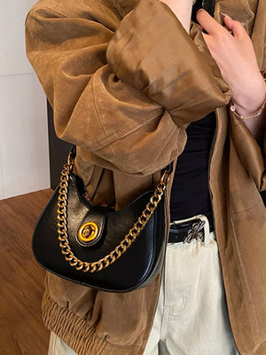 Black crescent mini shoulder bag with gold chain accent and clasp detail.