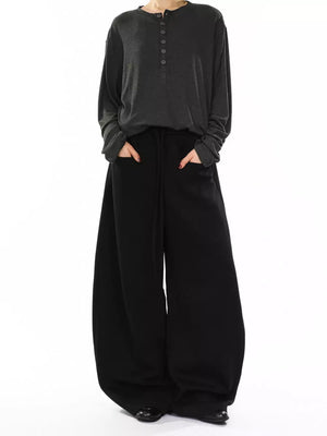 Black wide-leg sweatpants with drawstring and pockets, worn by a person in a gray long-sleeve shirt.