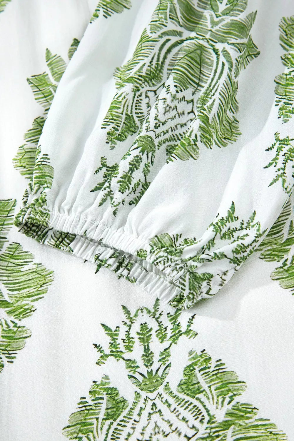 White mini dress with green floral print and elasticated cuff detail.