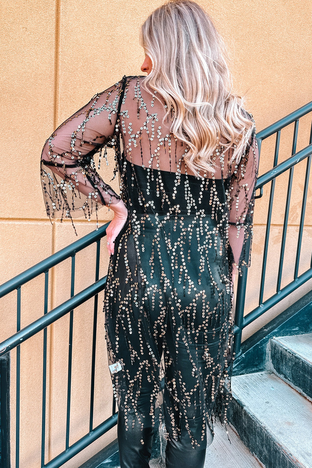 Black sequin duster with flared sleeves and fringe detail, worn over black pants.