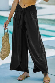 Black wrap-front palazzo pants with slit hem and tie waist detail.