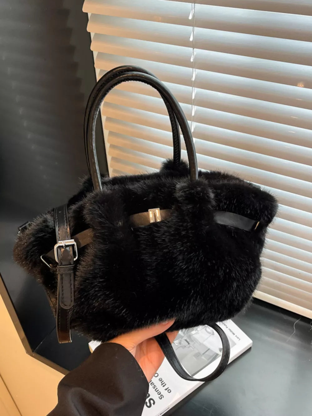 Black plush crossbody bag with chic buckle detail and top handles.
