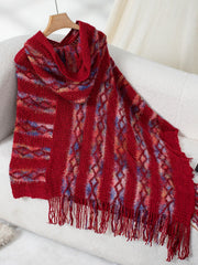 Textured knit hooded cape in red with diamond and stripe patterns and fringe detail.