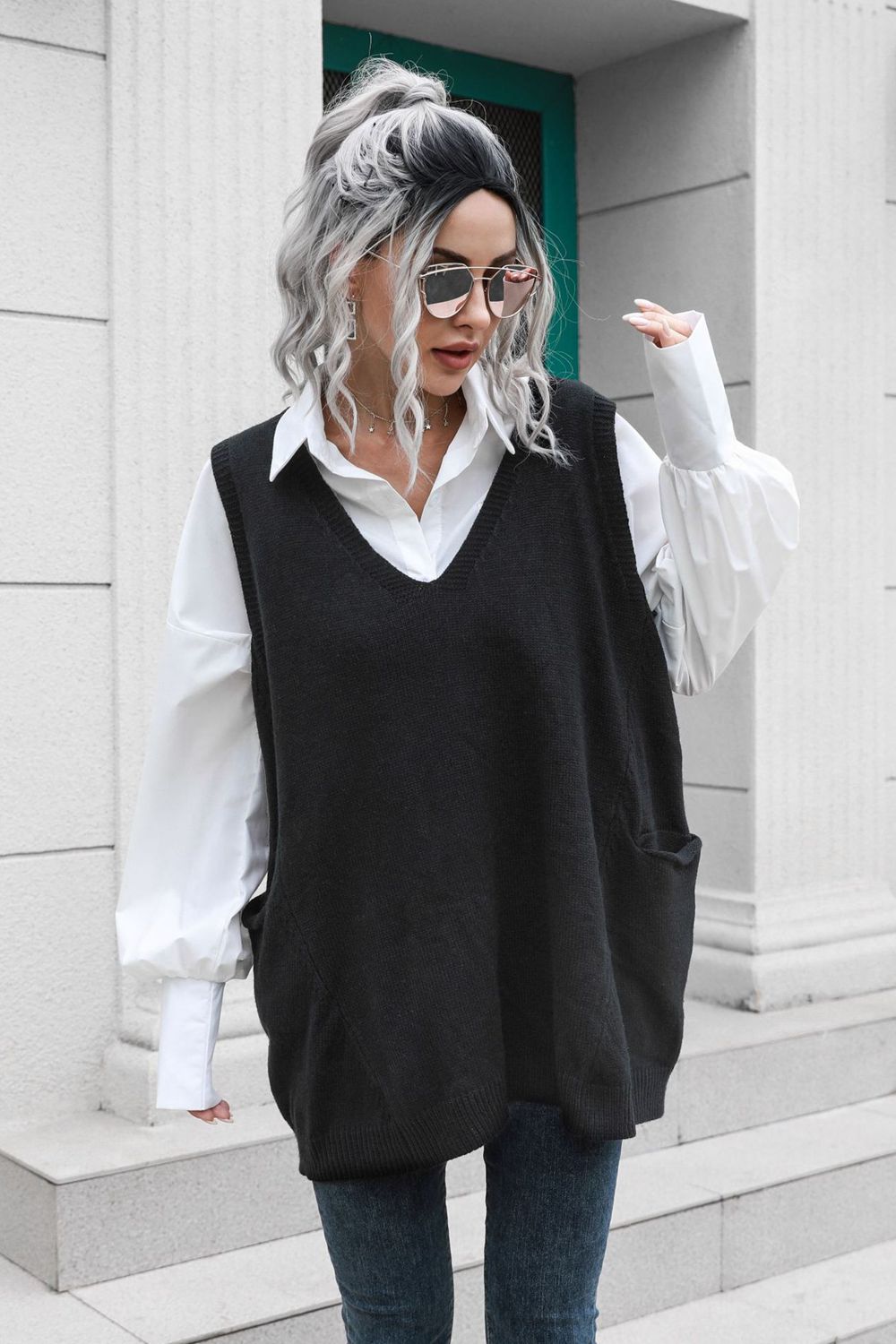 Black oversized knit vest with V-neck and pockets, styled over a white shirt.