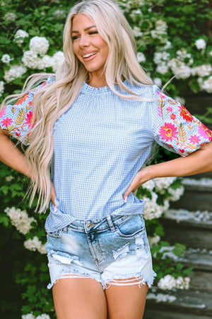 Light blue gingham blouse with embroidered floral puff sleeves and a ruffled neckline.