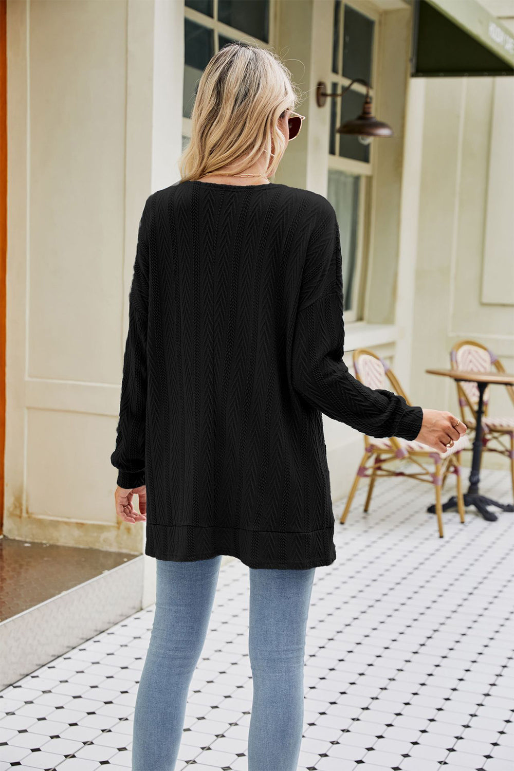 Black cable-knit cardigan with chevron pattern and pockets, styled with jeans.