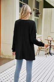 Black cable-knit cardigan with chevron pattern and pockets, styled with jeans.