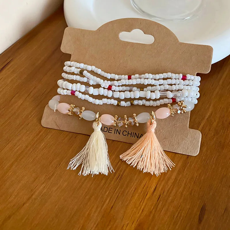 Beaded tassel stacked bracelet set with white beads, pink stones, and cream/peach tassels.