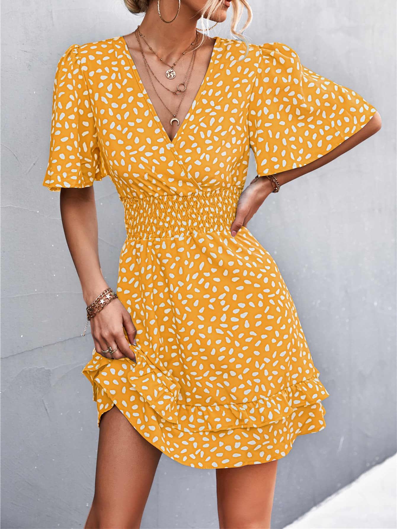 Mustard smocked waist mini dress with white speckle print, flutter sleeves, and ruffled hem.