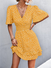 Mustard smocked waist mini dress with white speckle print, flutter sleeves, and ruffled hem.