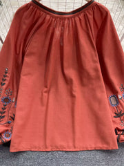 Orange red embroidered blouse with billowy sleeves and tie neck detail.