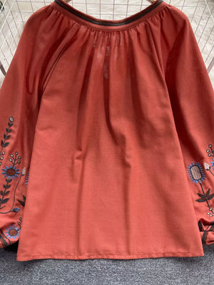 Orange red embroidered blouse with billowy sleeves and tie neck detail.
