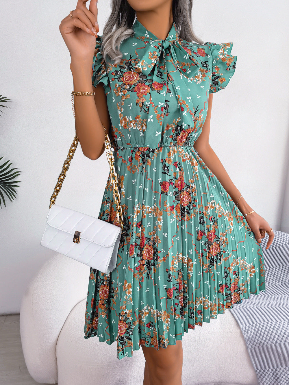 Turquoise floral mini dress with ruffle sleeves, bow neckline, and pleated A-line skirt.