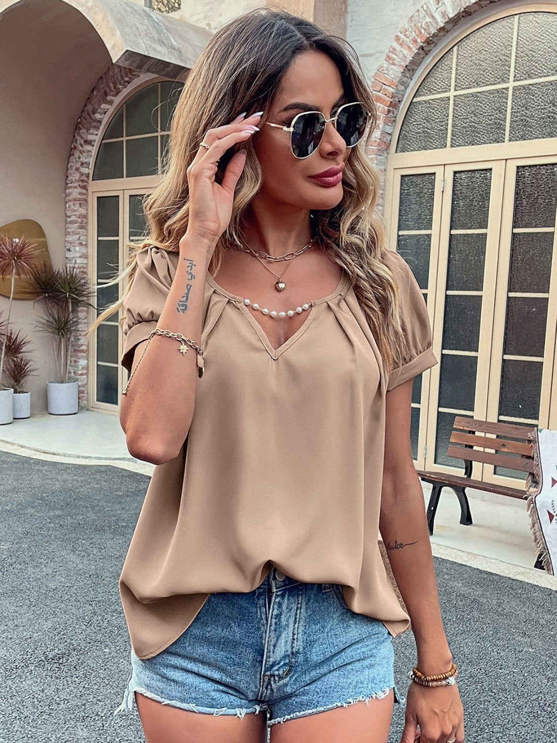 Camel gathered sleeve blouse with plunge neckline and pearl trim, styled with denim shorts.