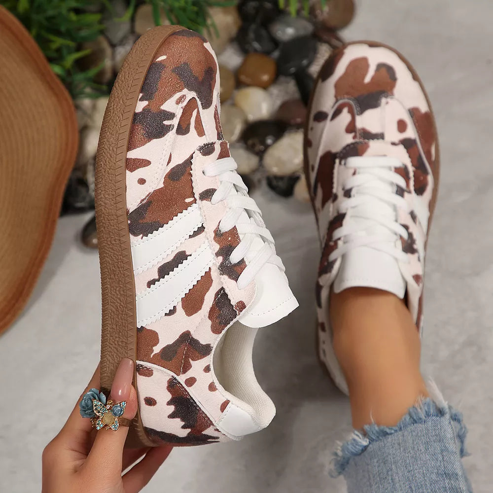 Brown and white cow print low-top sneakers with white laces and brown soles.