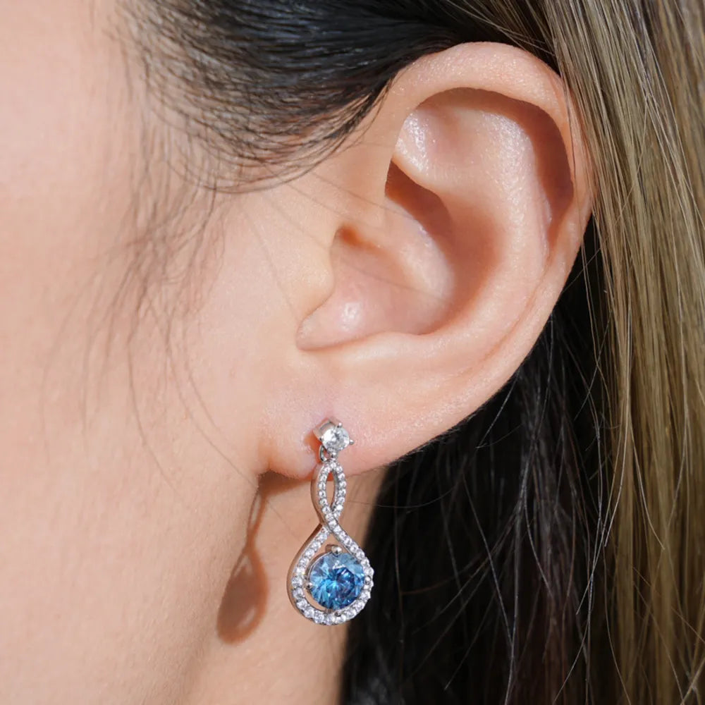 Infinity drop earrings with aquamarine and white stones on an ear.