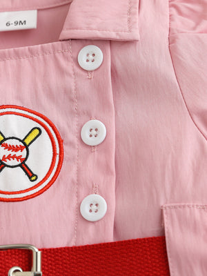 Pink cotton blend baseball dress for kids with embroidered baseball patch, white buttons, and red belt detail.