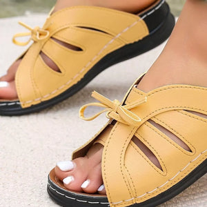 Yellow criss-cross wedge sandals with bow detail and cutouts.