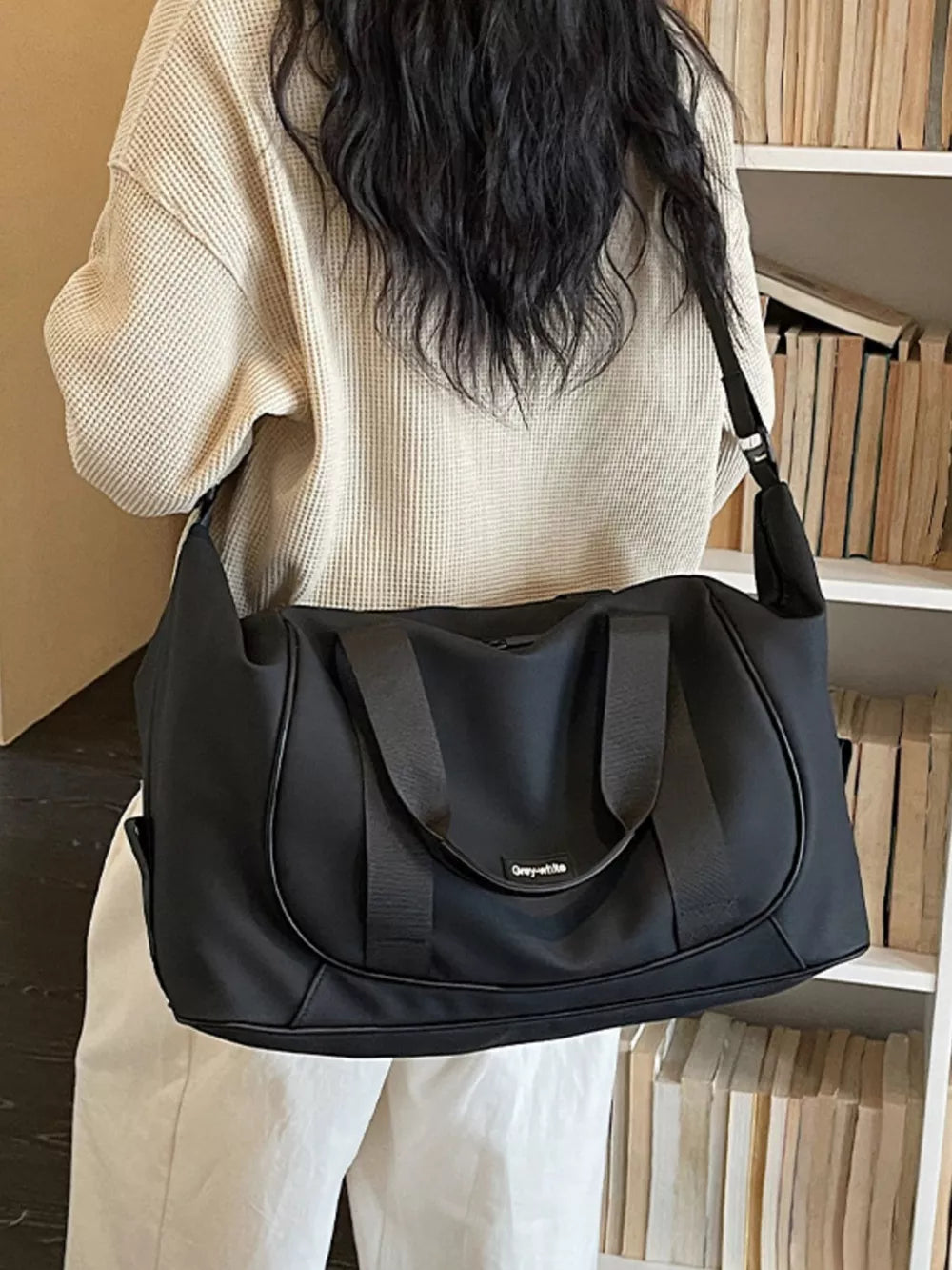 Black nylon travel duffle bag with curved stitching and adjustable strap, worn over the shoulder.
