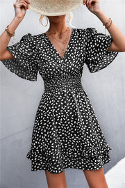 Black mini dress with white speckle print, V-neck, flutter sleeves, smocked waist, and ruffled hem.