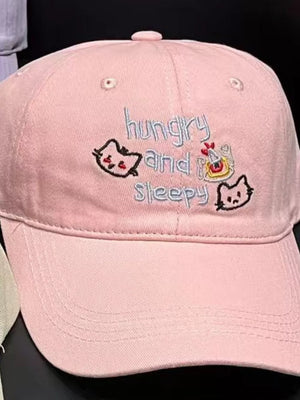 Light pink baseball cap with embroidered cats and text that reads hungry and sleepy.